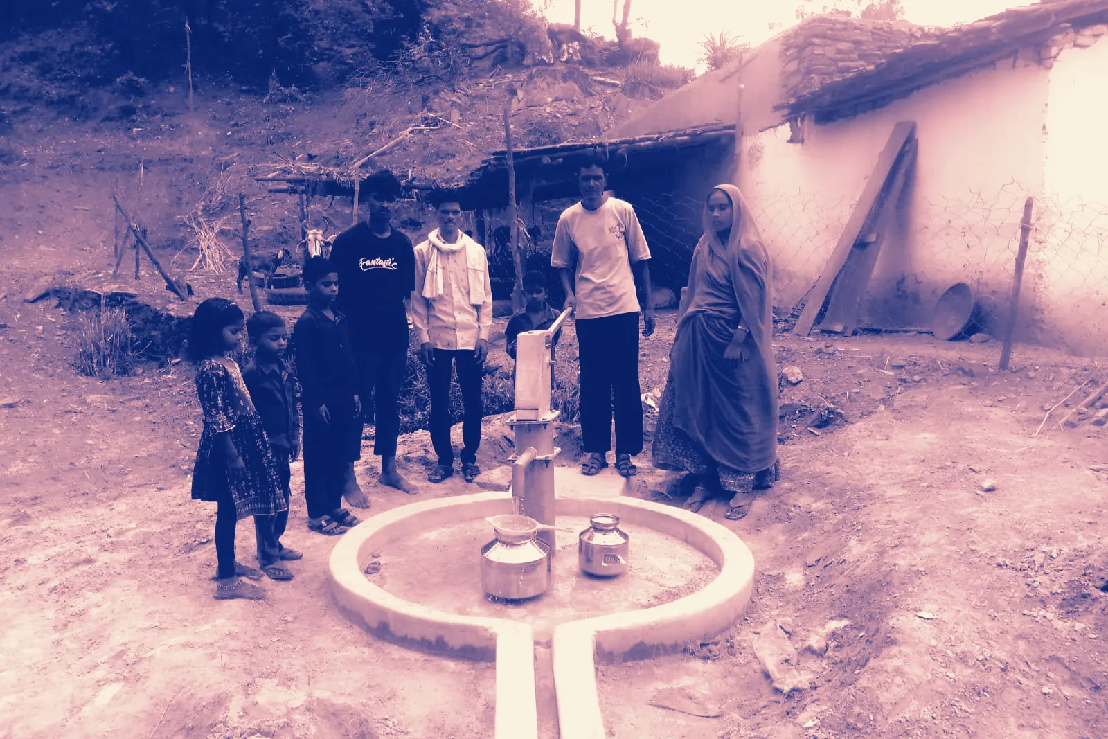 A family standing at the newly finished hand pump in their yard, water pots on the apron